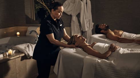 Two guests laying on massage tables in a room with a spa tub.