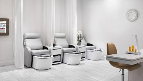 Nail salon with three light grey pedicure chairs, separate by white curtains, and one manicure station