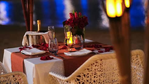 Table for two set with chilling champagne, flutes and a rose bouquet, aside torches and the gleaming reflection on the water.