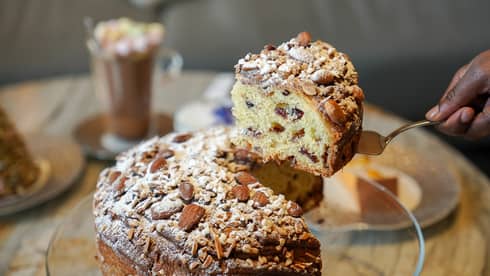 Hand holds up thick slice of powdered sugar?dusted panettone on gold cake server