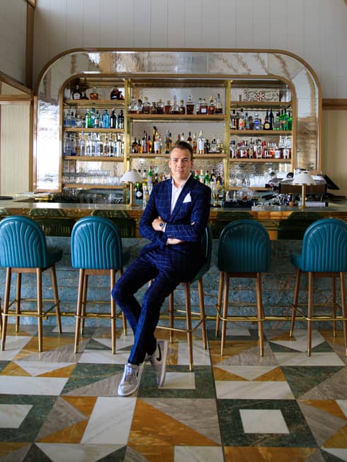 Restaurant Manager Cedric Vinckier in dark suit, seated with arms crossed in front of bar