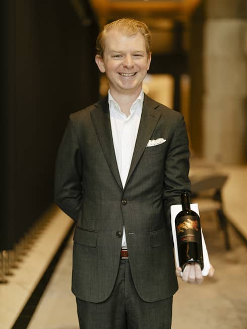 A man in a suit holding a bottle of wine.