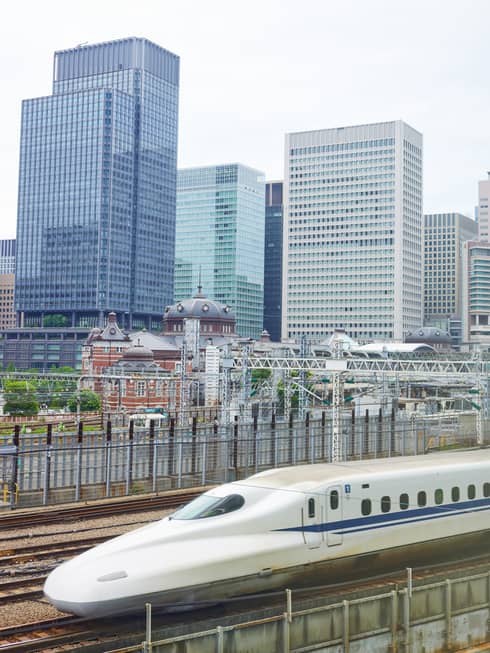 The Shinkansen bullet train speeds past Tokyo's railway station dwarfed by the skyline of rectangular, glass high-rises.