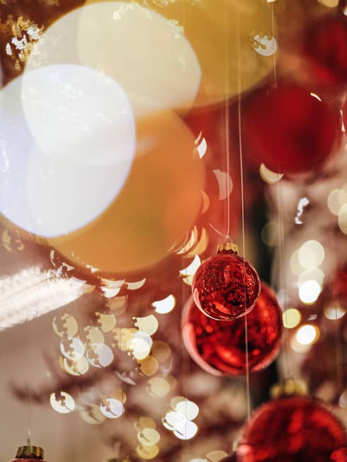 Close-up of red Christmas baubles hanging with blurred festive lights in the background