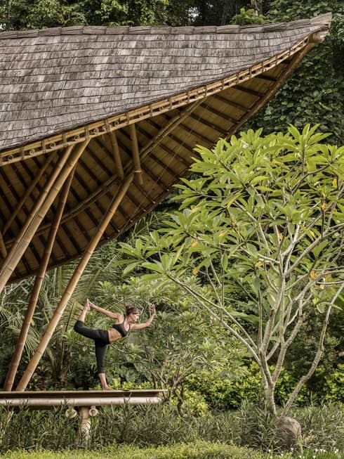 A guest with her arms and leg outstretched, doing yoga in an outdoor pavilion 
