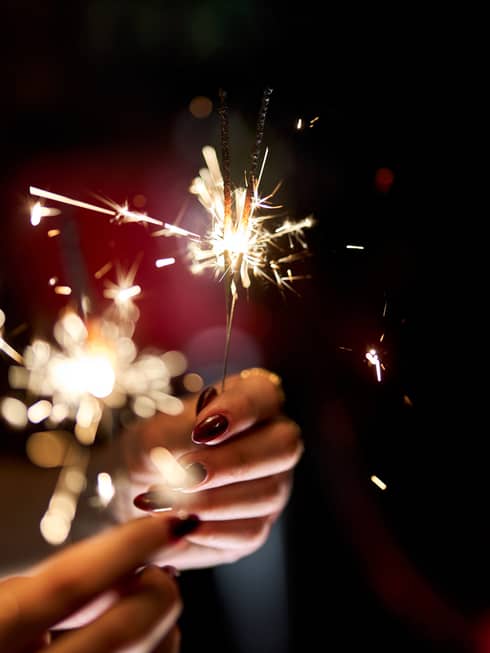 Hands holding a lit sparkler.