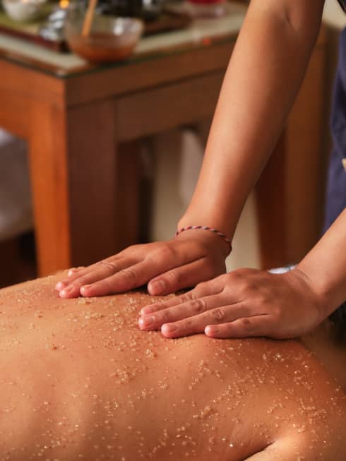 A spa attendant applies a scrub to a guest's back
