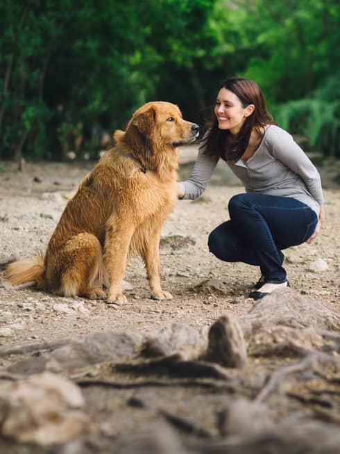 A woman petting a dog outside at a park trail.