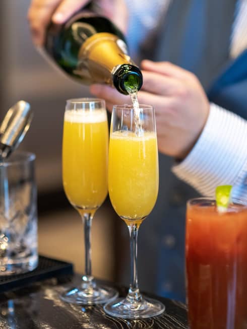 A person pouring a beverage from a bottle into two glasses