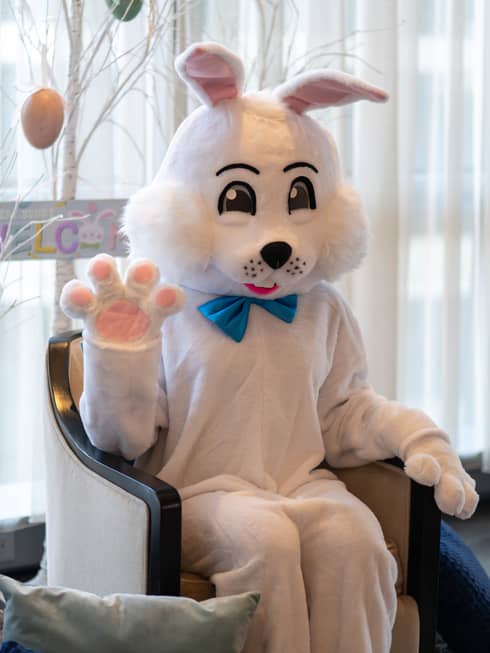 A person wearing an Easter Bunny costume and sitting near a tree decorated with Easter eggs