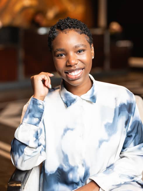 Nalany Guerrier sitting in a chair while wearing a blue and white collared shirt.