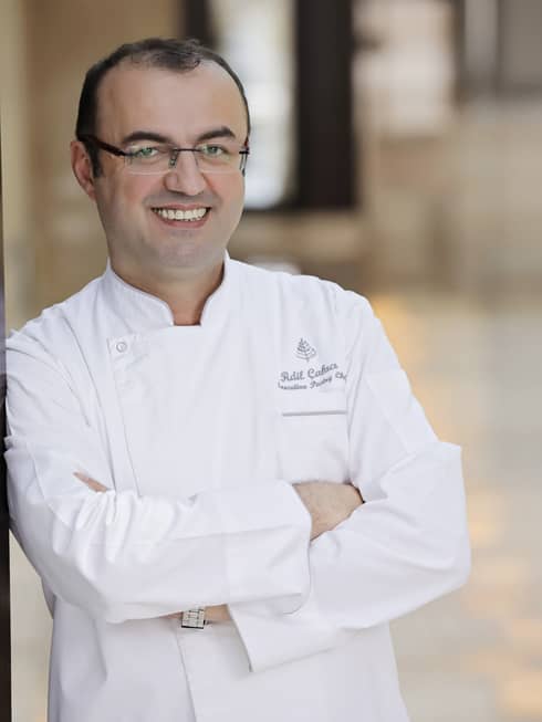 A portrait of Chef Adil Çakıcı leaning against a cream wall