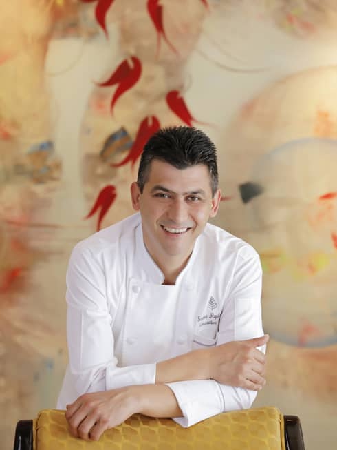 A portrait of Chef Savaş Aydemir leaning against a yellow chair