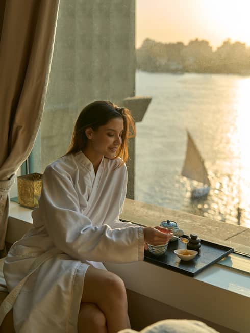 Woman in Four Seasons robe enjoys tea by the window at sunset