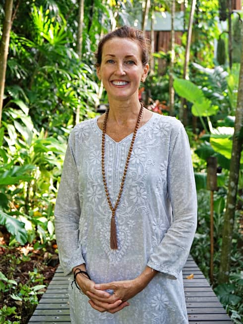 A smiling Carol Kandell wearing a long-sleeved patterned dress and long, beaded necklace