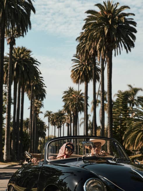 A couple drives down a palm tree?lined street in a black vintage convertible