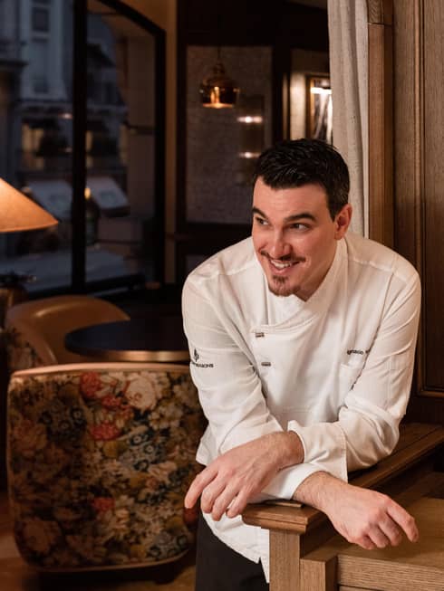 Chef Ignacio Vara in white chef's coat, leaning on pony wall with with wrists crossed