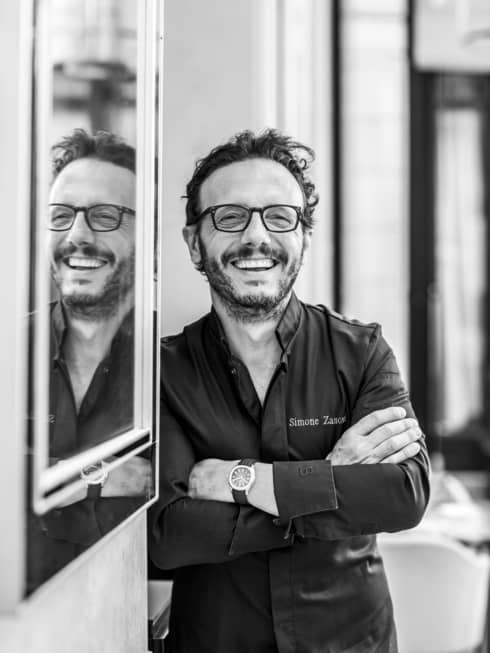 Shot of Chef Simone Zanoni, smiling next to a wall with mirror
