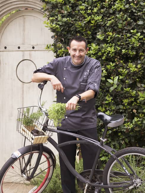 Executive Chef Marco Fossati in uniform with bicycle, fresh herbs in basket
