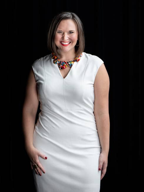 A woman in a white dress and colourful necklace.