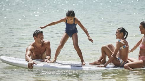 A family sitting on a large surf or paddleboard.