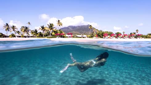 Underwater view of woman swimming with flippers, beach and resort on shore above