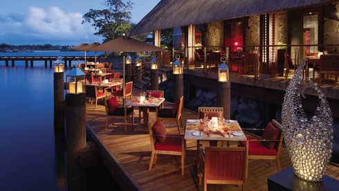 Outdoor dining tables on a pier overlook the waters.
