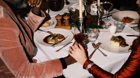 Two guests sitting at a dining table holding hands and a glass of wine.