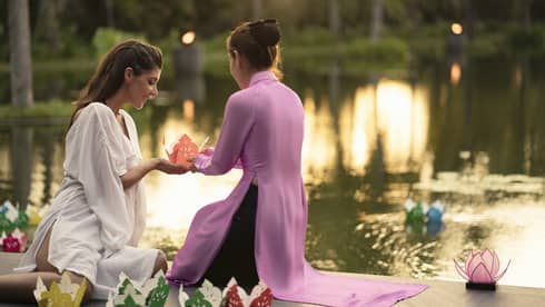 Two women prepare to release paper boat with love letter onto lotus pond