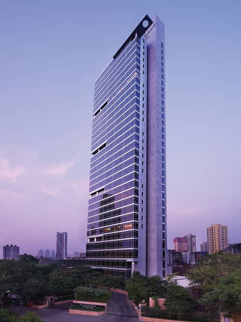 Four Seasons Hotel Mumbai glass tower exterior with trees around entrance, sign