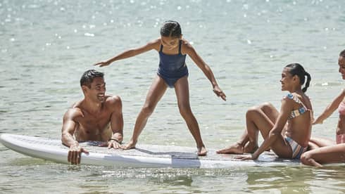 A family sitting on a large surf or paddleboard.