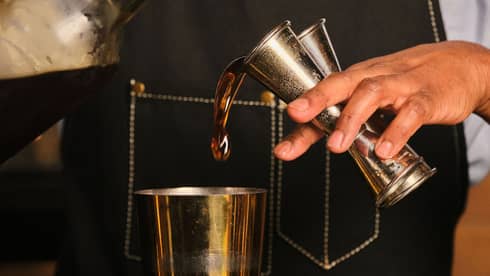 A bartender pours liquid from two jiggers into a cocktail shaker