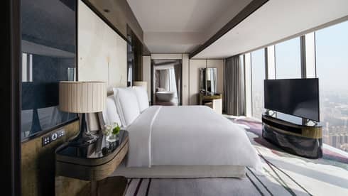 Deluxe King River View Suite with bed and white linens, floor-to-ceiling windows