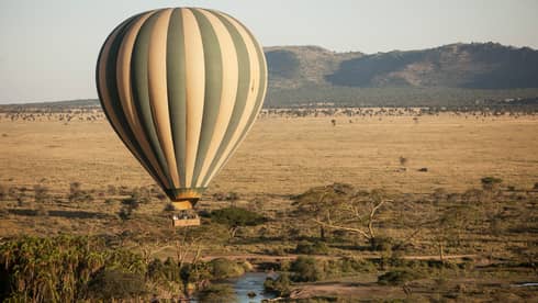 Striped hot air balloon hovers over Serengeti field