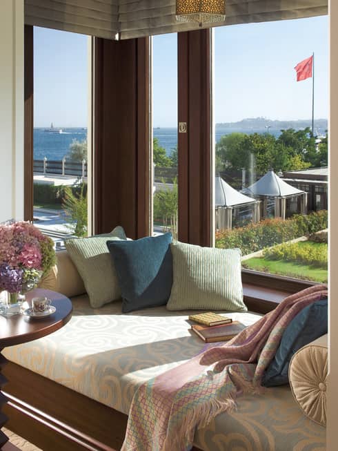 Cushioned bench with pillows, table in front of large bay window overlooking patio