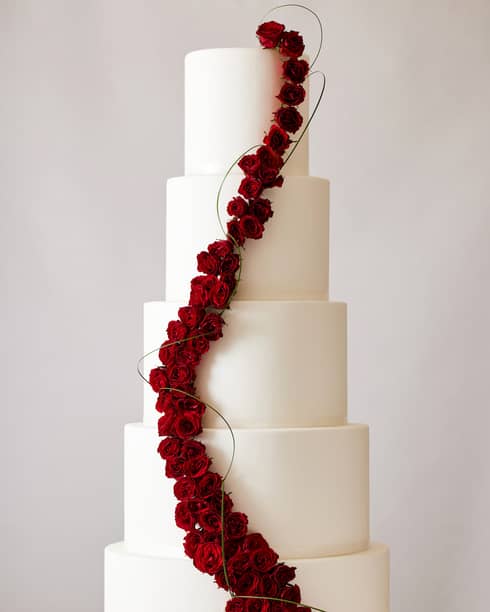 Five-tiered white wedding cake with a line of dark red roses cascading from top to bottom