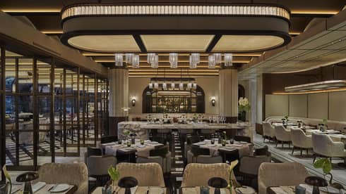 Restaurant dining room with grey and cream colour palatte, green florals on every table and a large overhead curved light piece