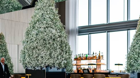 A dining area with beige chairs and place mats, Christmas trees and a bar can be seen on the other side of the room.