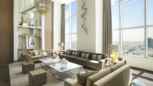 Kingdom Suite with tall ceilings and windows, three sofas, two chairs and coffee tables, large chandelier and wall sculpture