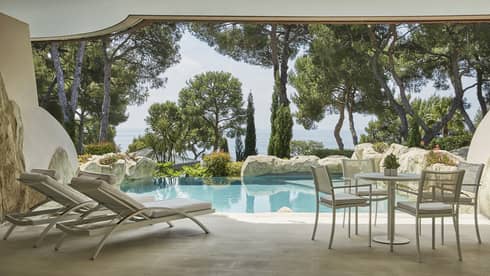 Private stone pool and terrace with two lounge chairs, table and chairs, sea view through greenery