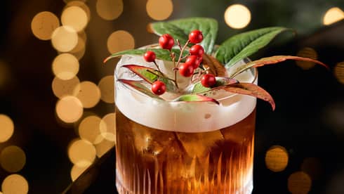 A cocktail with small red berries and green leaves as a garnish.
