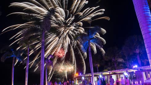 People around resort outdoor pool/bar watching fireworks in the night sky
