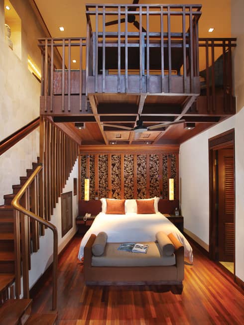 Resort room bed and bench beside winding wood staircase leading to second-level loft