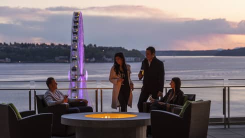 Group on the patio at Four Seasons Hotel Seattle at sunset, with Elliott Bay, the Great Wheel and a ferry in background