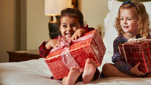 Two young girls sitting on a bed with large gift boxes.