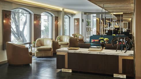 White marble counter with books, horse statue, light brown leather bucket armchairs line windows