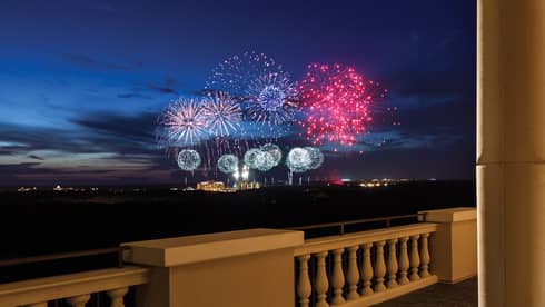 The terrace of a restaurant with tables and people watching fireworks in the distance.