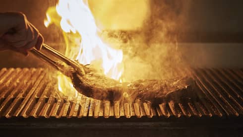Several steaks being grilled over an open fire.