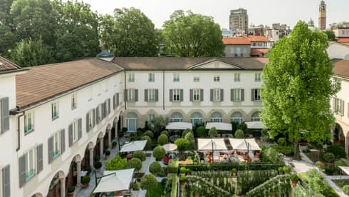 Aerial view of a hotel courtyard, featuring a lush garden, outdoor dining areas and a historic building with arched walkways