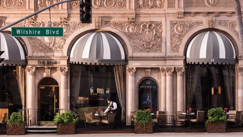 Server sets table on street-side patio outside hotel, Wilshire Blvd street sign